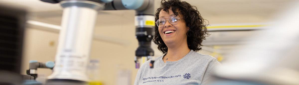 A student smiles while working on a manufacturing robot in Pima's AIT lab